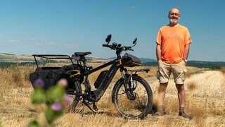 älterer Herr steht vor Trekkingrad in einem Feld
