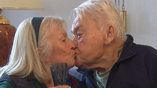 Eine Frau mit weißen Haaren und ein Mann mit weißen Haaren geben sich einen Kuss.