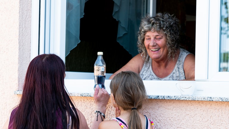 Frau steht am Fenster und redet mit einer anderen Frau und einem Kind über die Fensterbank.
