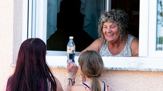 Frau steht am Fenster und redet mit einer anderen Frau und einem Kind über die Fensterbank.