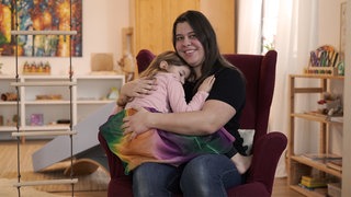 Frau mit braunen Haaren mit Kind auf dem Schoß.