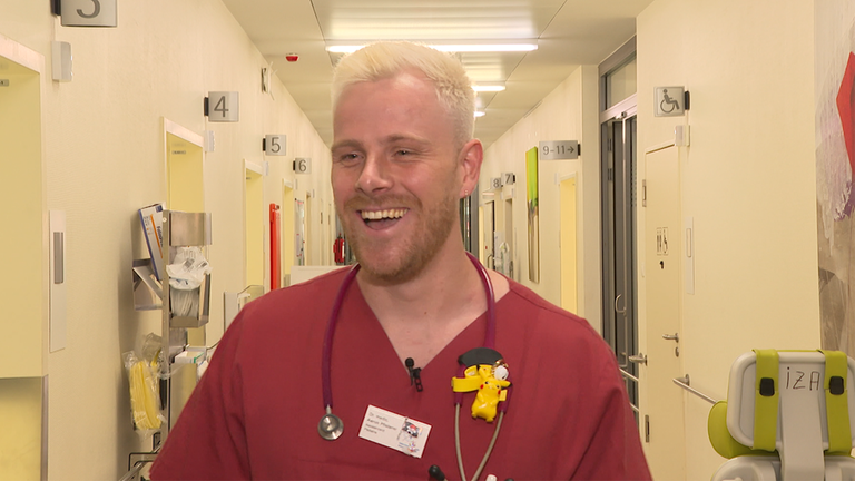 Aaron, angehender Kinderarzt, mit seinem Kittel in einem Krankenhausflur. 