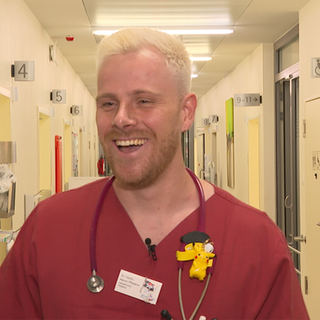 Aaron, angehender Kinderarzt, mit seinem Kittel in einem Krankenhausflur. 