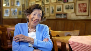 Eine alte Frau lacht in die Kamera. Inge betreibt mit 88 noch immer ihre Weinstube "Narrenstübchen" und ist damit die älteste Gastwirtin in Speyer.