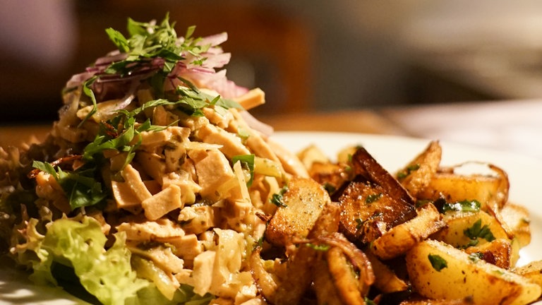 Auf einem Teller liegen fein angerichtet Wurstsalat und Bratkartoffeln.