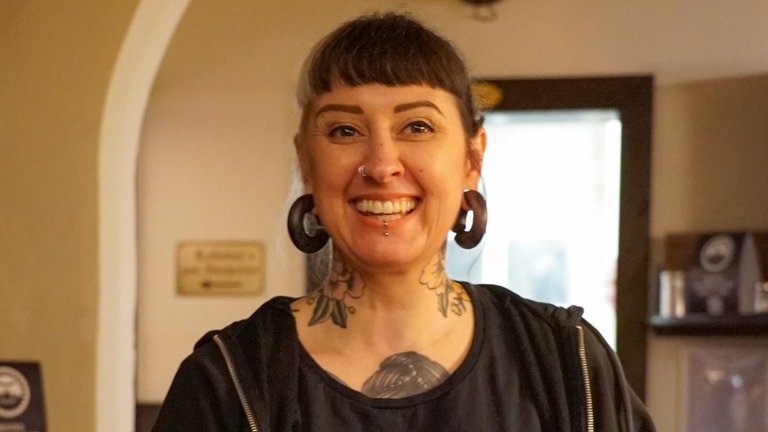 Junge Frau mit schwarz-weißen Haaren und T-Shirt mit Eule serviert Essen.