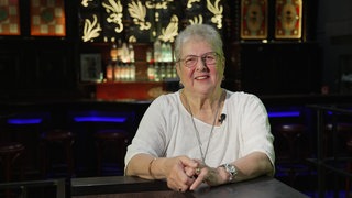 Seniorin sitzt an einer Theke und lächelt in die Kamera