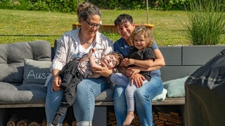 Eine Familie auf einer Garten Couch. Zwei Frauen haben jeweils ein Kind auf dem Schoß.