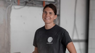 Junge Frau mit braunen, zusammengebundenen Haaren, lächelt in die Kamera.