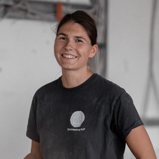 Junge Frau mit braunen, zusammengebundenen Haaren, lächelt in die Kamera.