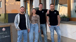 Eine junge Frau und drei junge Männer vor einer Kneipe.