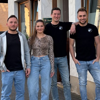 Eine junge Frau und drei junge Männer vor einer Kneipe.