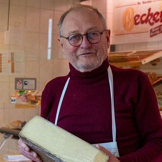 Ein Verkäufer hält einen Laib Käse in der Hand. Hanns wagt mit 63 einen Neuanfang und eröffnet einen Käseladen.