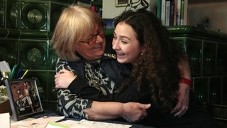 Eine ältere Frau und eine junge Frau umarmen sich und lachen.