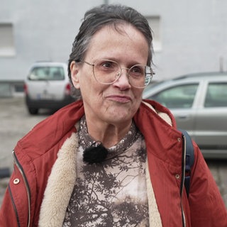 Dame mit einer roten Winterjacke und kurzen braunen Haaren und roter Jacke steht auf einem Hinterhof-Parkplatz.