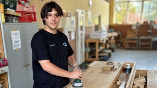 Junger Mann mit braunen Haaren schleift ein Stück Holz.