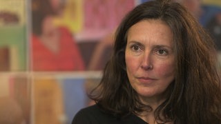 Eine Frau mit braunen Haaren mit entschlossenem Blick schaut nach vorn