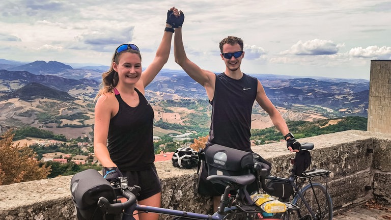 Zwei junge Menschen, mit ihren Fahrrädern, klatschen sich in die Hände. 