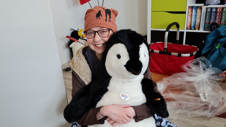 Junge Frau, die auf dem Boden sitzt und einen großen Pinguin in den Armen hält.