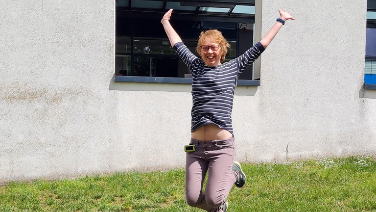 Junge Frau, die auf einer Wiese in die Luft springt und fröhlich ist.