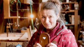 Frau mittleren Alters, mit kleiner Wichteltür in ihrer weihnachtlichen Werkstatt