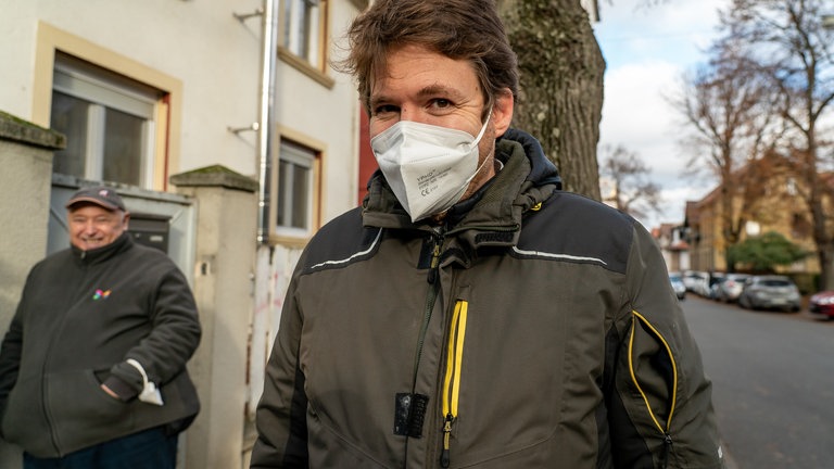 Mann mit Maske, vor Baum.