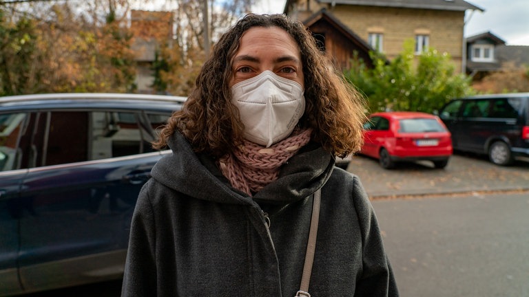 Frau mit Maske steht auf der Straße.