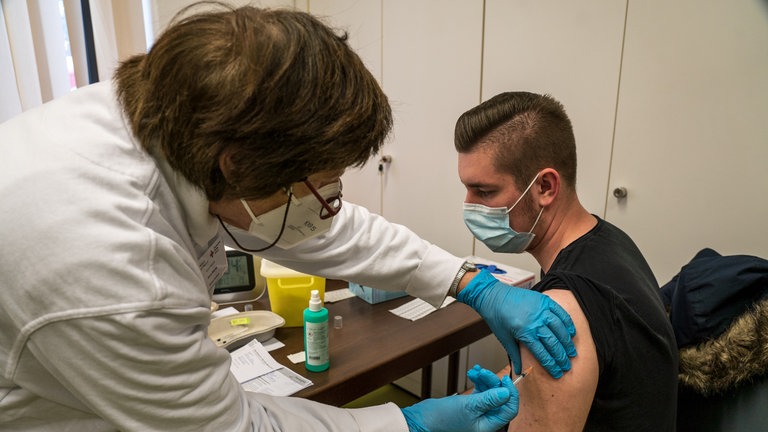 Mann auf Stuhl bekommt Spritze von Ärztin.