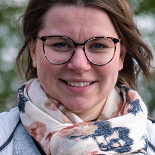 Junge Frau mit braunen Haaren, Melissa, steht vor herbstlichem Hintergrund