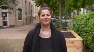 Junge Frau in schwarz gekleidet auf einem Gehweg in einem Altbauwohngebiet