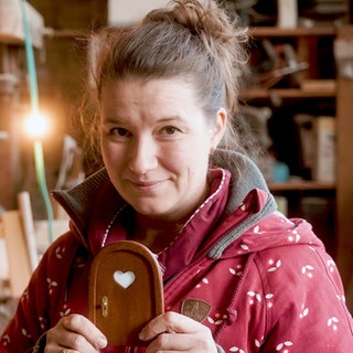 Elli, mittelalte Frau mit braunen Haaren in einer Holzwerkstatt.