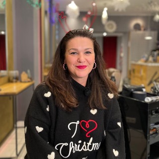 Frau mit braunen Haaren und Weihnachtspullover in ihrem Friseursalon sitzend
