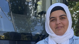 41 Jährige Frau steht mit verschränkten Armen vor einer Straßenbahn