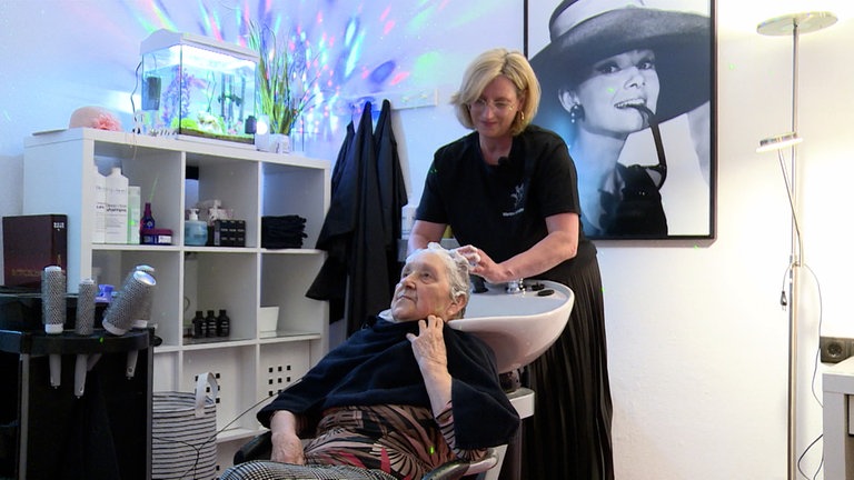 Friseurin wäscht einer Seniorin die Haare.