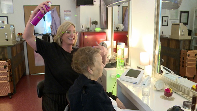 Friseurin sprüht Haarspray auf die Frisur ihrer Kundin.