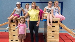 Blonde Frau lächelt in die Kamera, gemeinsam mit Kindern.