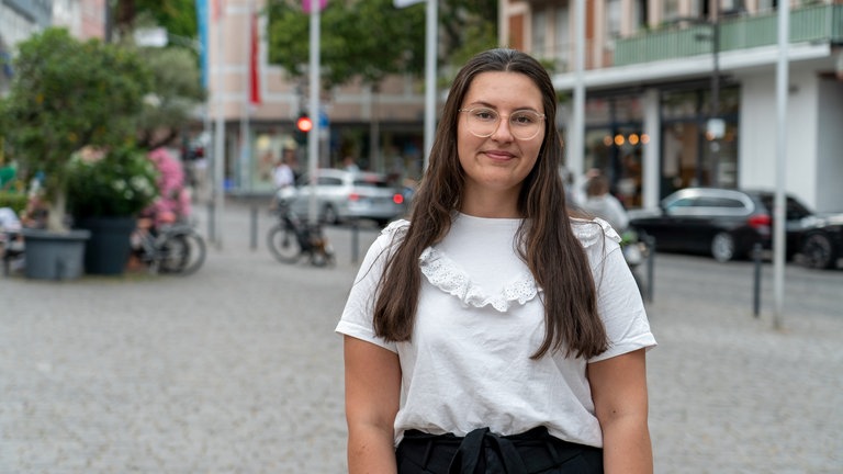Eine junge Frau mit Brille steht auf dem Wormser Marktplatz und lächelt in die Kamera.