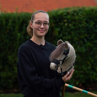 Nele, junge Frau, reitet auf einem Steckenpferd