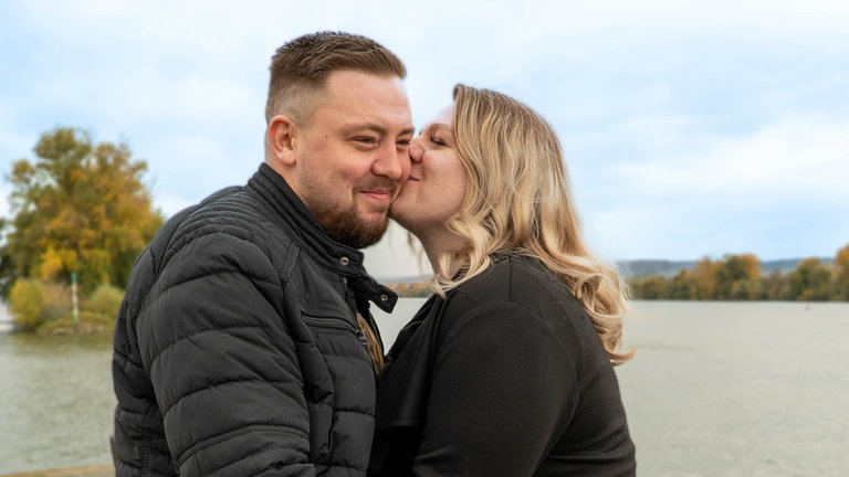 Junges Paar steht am Rhein und küsst sich.