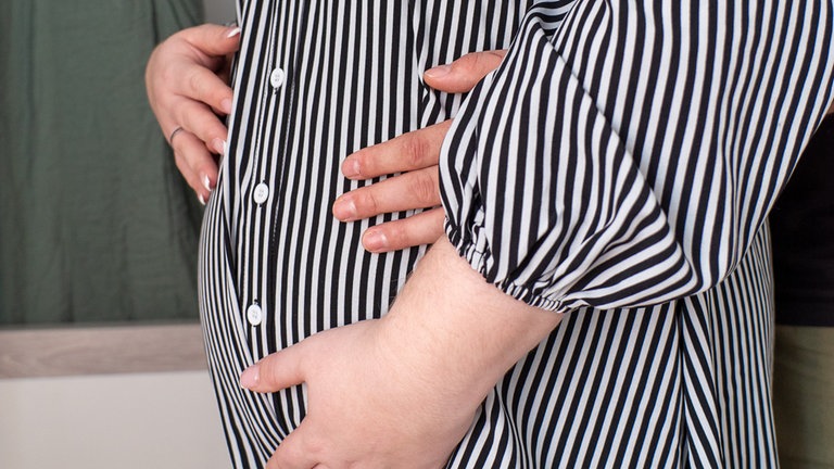 Hände liegen auf dem Babybauch von junger Frau.