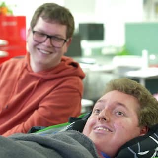 Zwei junge Männer – einer liegend, einer sitzend – arbeiten in einer Behindertenwerkstatt