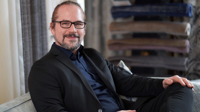 Ein Mann mit grauen langen Haaren mit Brille lächelt in die Kamera