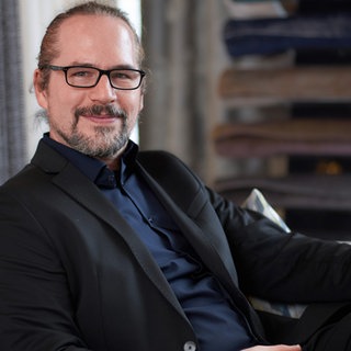 Ein Mann mit grauen langen Haaren mit Brille lächelt in die Kamera