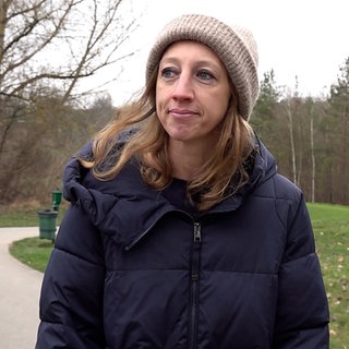 Eine Frau steht mit Mütze und Wintejacke auf einem Feldweg.
