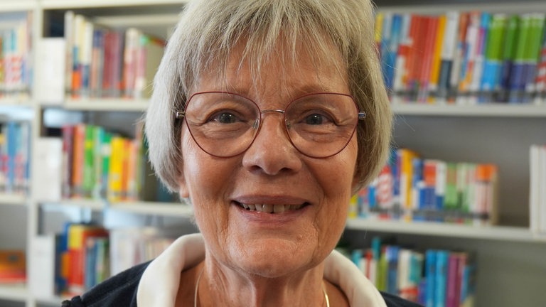 Ältere Damen, mit kurzen Haaren, magentafarbenem Pullover und weißer Bluse. 