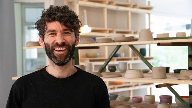 Mann mit schwarzen Locken lächelt in Kamera.