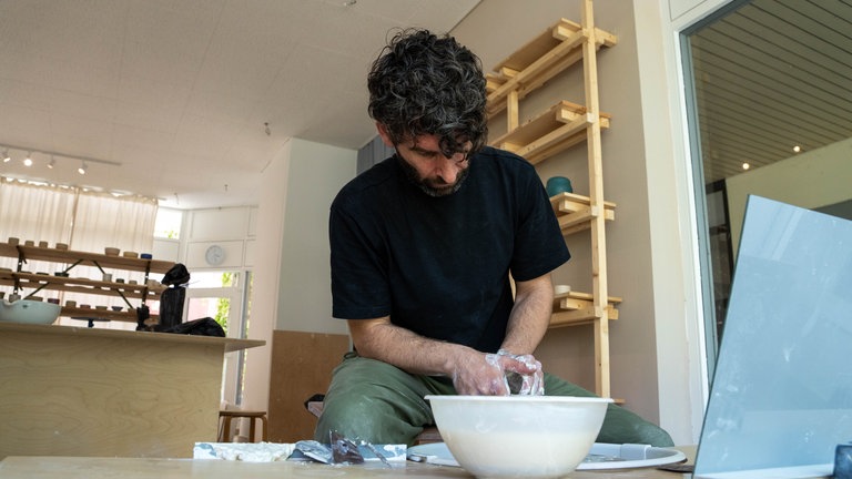 Mann schaut nach unten zu einer Töpferscheibe an der er gerade arbeitet.