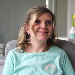 Frau mit blonden Haaren und türkisem T-Shirt lächelt in Kamera.