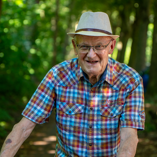 Älterer Herr mit Hut und kariertem Hemd im Wald