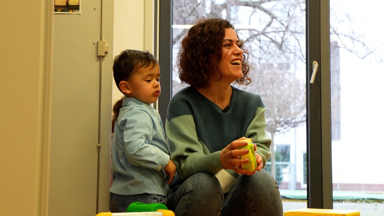 Frau sitzt mit ihrem Sohn auf dem Boden und lacht